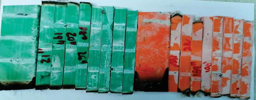 Green and red fibreglass laminate test strips, slightly charred at the ends after a flammability test