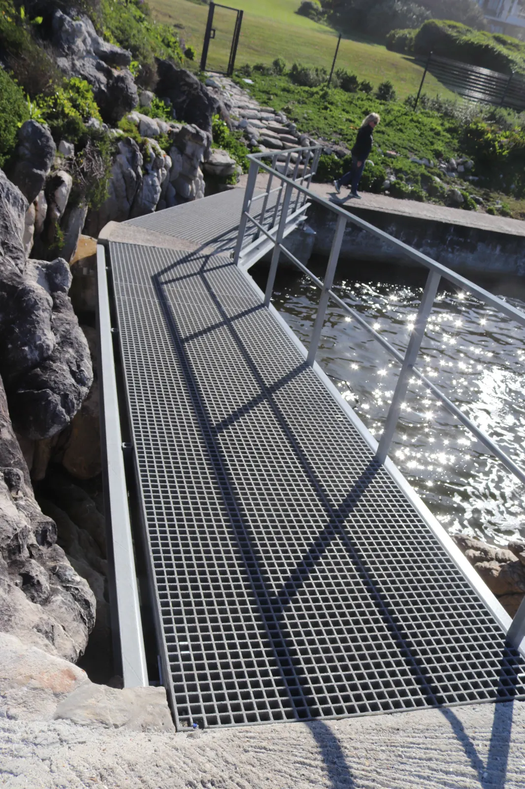 Fibreglass grating walkway along a rocky shore, with water and grass beyond