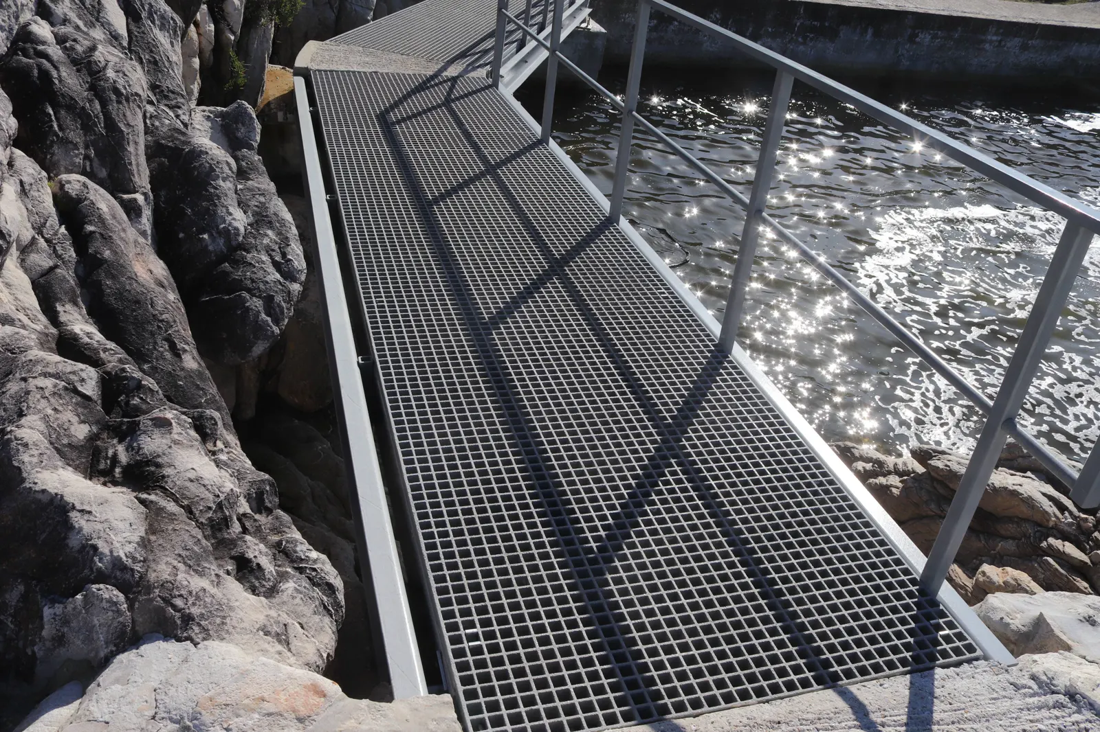 Fibreglass grating walkway with a steel handrail along rocks beside the water